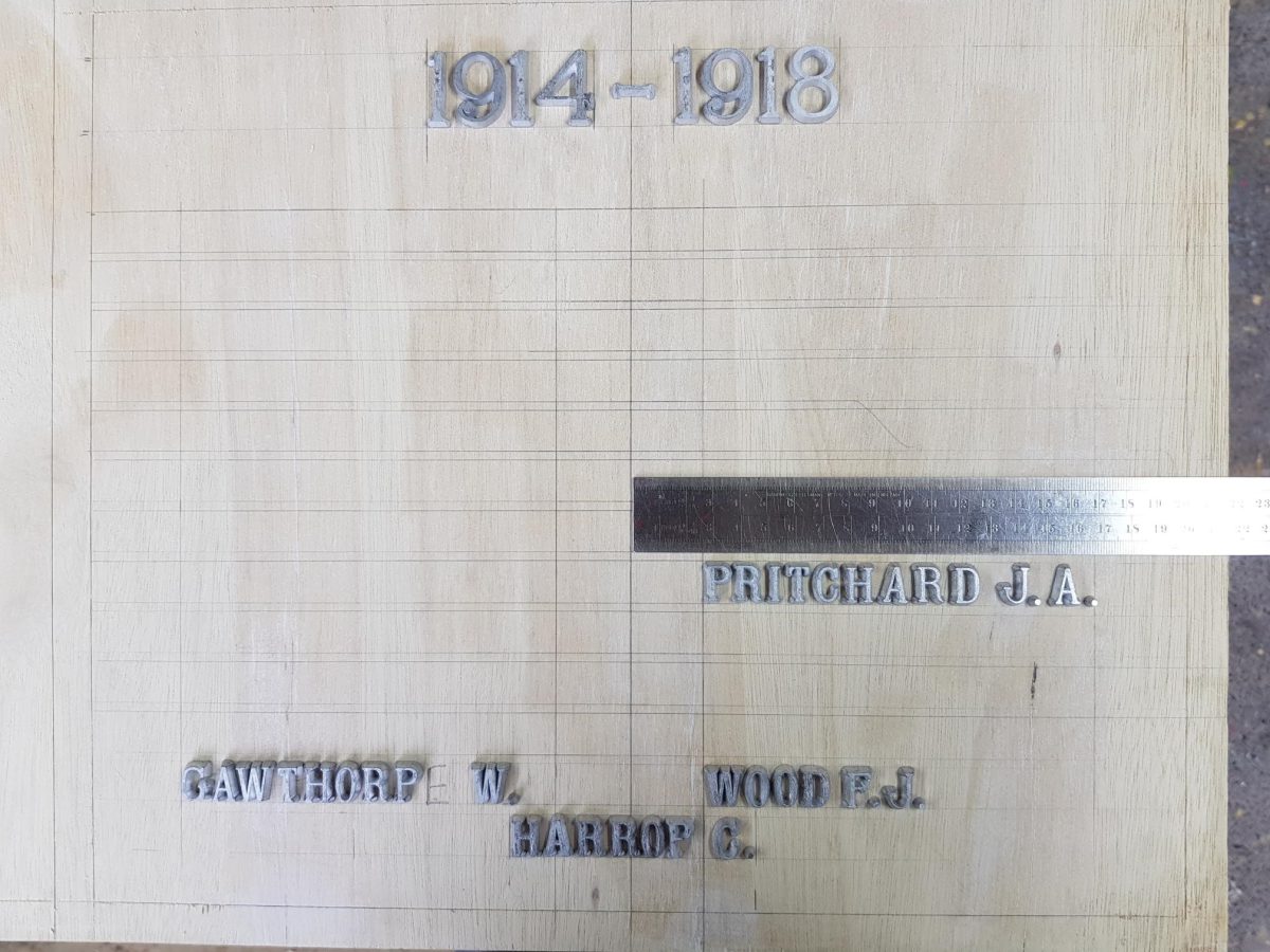 A photograph of Calibre Metalwork's patternmaker in the process of crafting individual letters and hand setting the type on Old Colwyn Memorial.