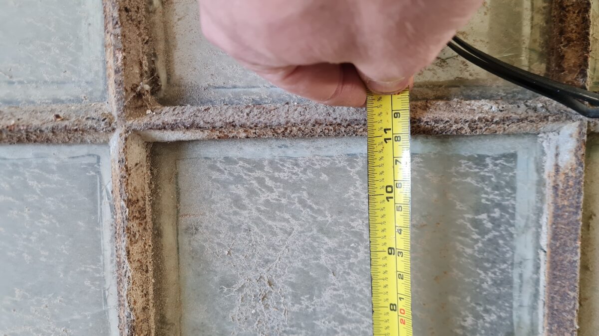 A photograph of someone measuring the slender glazing bars of original iron salvaged window frames.